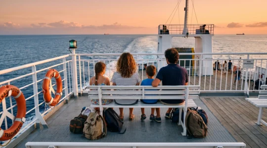 Famiglia italiana di quattro persone seduta sul ponte aperto di un traghetto moderno durante la navigazione pomeridiana nel Mediterraneo, osservando il tramonto sul mare calmo con bagagli accanto, atmosfera rilassata e serena.